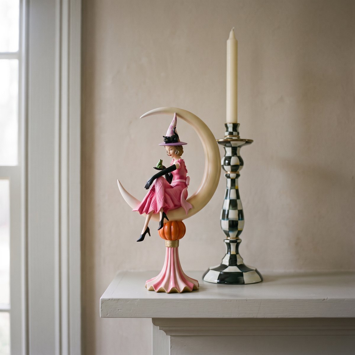 Glam 'O' Ween Witch on Moon figurine on a mantel shelf beside a large Courtly Check enamel candlestick, seen from below at seated eye level
