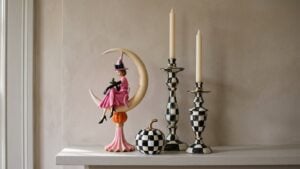 MacKenzie-Childs Halloween mantel styled with the Glam 'O' Ween Witch on Moon figurine, two Courtly Check enamel candlesticks and a Courtly Check glossy mini pumpkin on a white mantel shelf