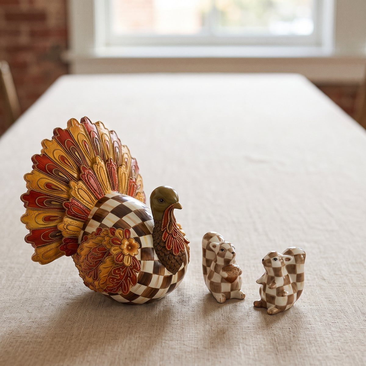 The MacKenzie-Childs Harvest Glow Aurora Turkey with the Mocha Check Squirrel Salt and Pepper Set clustered beside it at one end of a table, the rest of the table left clear.