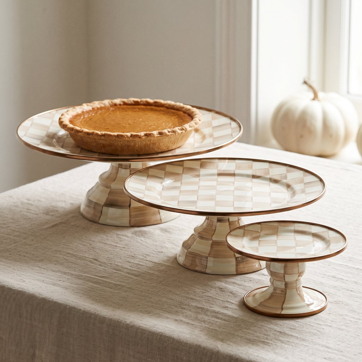 MacKenzie-Childs Mocha Check Large, Small and Mini Pedestal Platters grouped at three heights with a pumpkin pie on the large pedestal