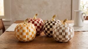 Amber Check, Paprika Check, Chocolate Check and Mocha Check medium pumpkins from MacKenzie-Childs grouped on a wooden dining table in warm autumn daylight