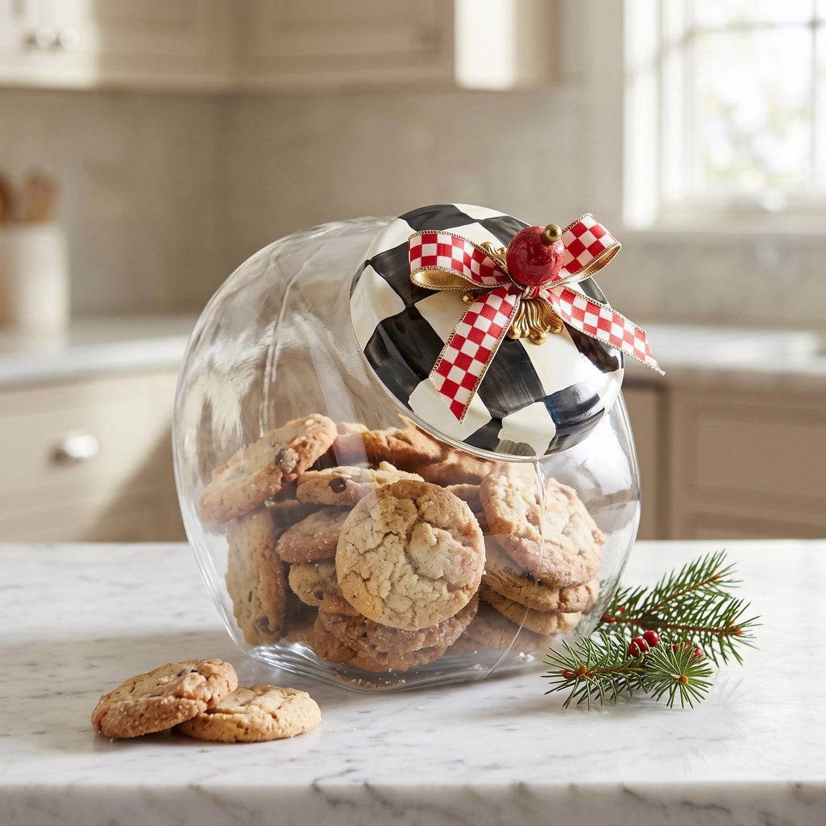 Glass cookie jar with a black and white check lid and a red check ribbon bow tied at the knob, filled with cookies on a white marble counter