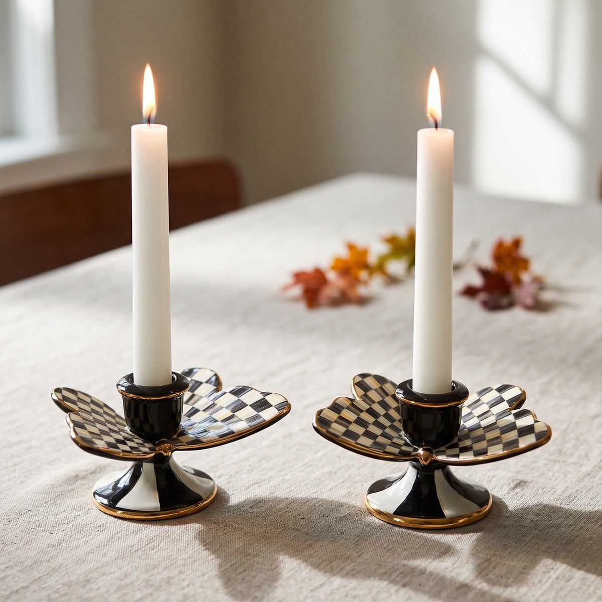 Pair of Courtly Check butterfly candle holders with gold-edged checked wings, each holding a lit white taper on a linen tablecloth